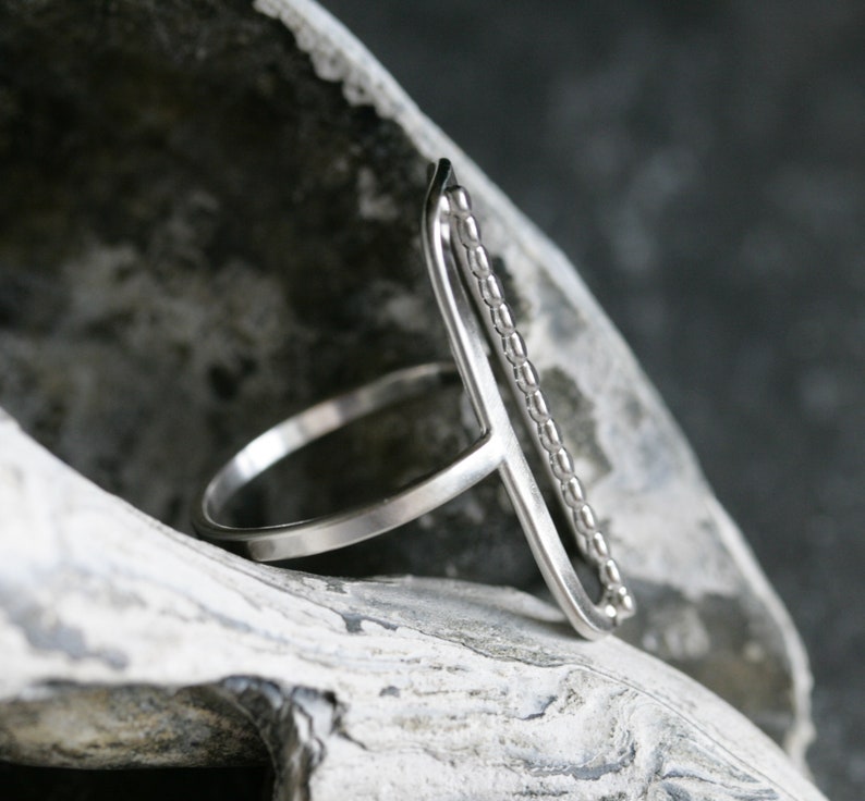 K&ouml;nnte beinhalten: Ein silberner Ring mit einer strukturierten Band und einem geraden, offenen Design. Der Ring ist aus Metall und hat einen minimalistischen Stil.