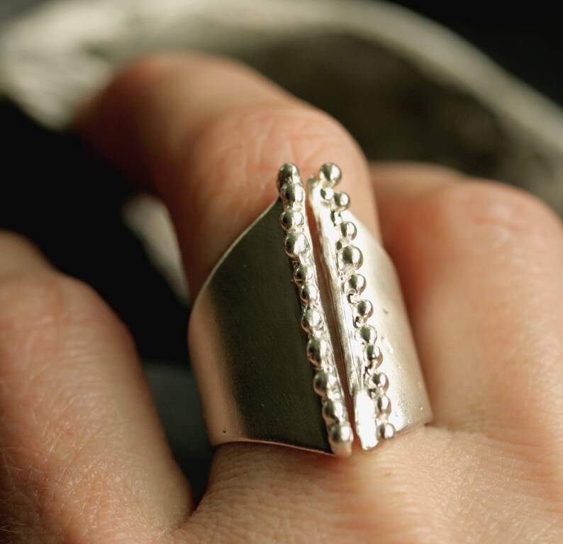 May include: A silver ring with a unique design featuring two vertical rows of beads on either side of a smooth, flat band.