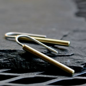May include: A pair of minimalist earrings with a simple, modern design. The earrings are made of brass and silver, and have a curved, hook-like shape.