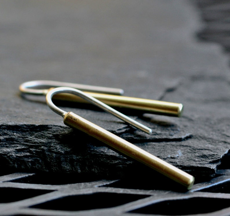 May include: A pair of minimalist earrings with a simple, modern design. The earrings are made of brass and silver, and have a curved, hook-like shape.