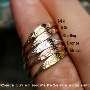 May include: Five stacking rings with a sunburst design. The rings are made of different metals, including 14k gold, 10k gold, sterling silver, bronze, and brass.