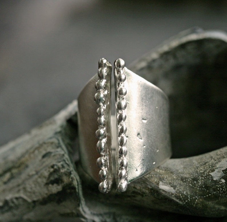 May include: A silver ring with a textured band and two rows of small beads on each side.