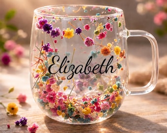 Könnte beinhalten: Ein klarer Glasbecher mit doppelwandigem Design, gefüllt mit kleinen, bunten Trockenblumen in Rosa, Gelb, Violett und Blau. Der Name Elizabeth ist in einer schwarzen Schreibschrift auf der Vorderseite des Glasbechers aufgedruckt.