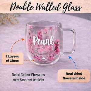 K&ouml;nnte beinhalten: Ein transparenter doppelwandiger Glasbecher mit rosa Trockenblumen, die zwischen den beiden Glasschichten versiegelt sind. Das Wort Pearl ist in wei&szlig;er Schreibschrift aufgedruckt. Textetiketten weisen auf 2 Layers of Glass und Real Dried Flowers hin.