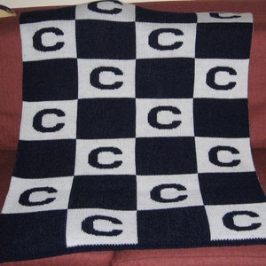 May include: A navy blue and white checkered blanket with the letter "C" woven into each square.