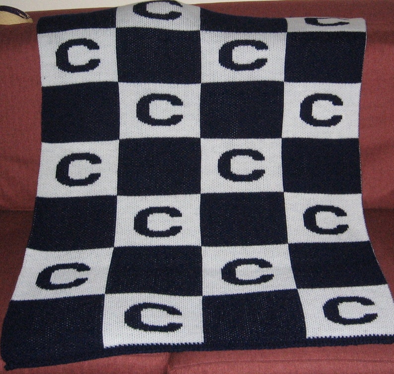 May include: A navy blue and white checkered blanket with the letter "C" woven into each square.