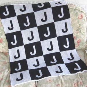 May include: A black and white checkered baby blanket with the letter "J" repeated throughout the design.