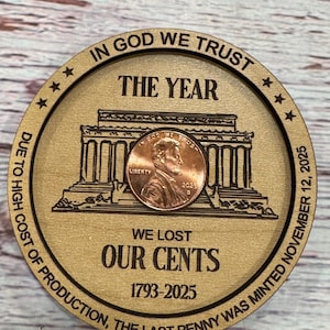 May include: A wooden round with engraved text and a penny. The text reads "IN GOD WE TRUST," "THE YEAR," and "WE LOST OUR CENTS 1793-2025." A penny is centered on the wooden round, with the image of Abraham Lincoln.