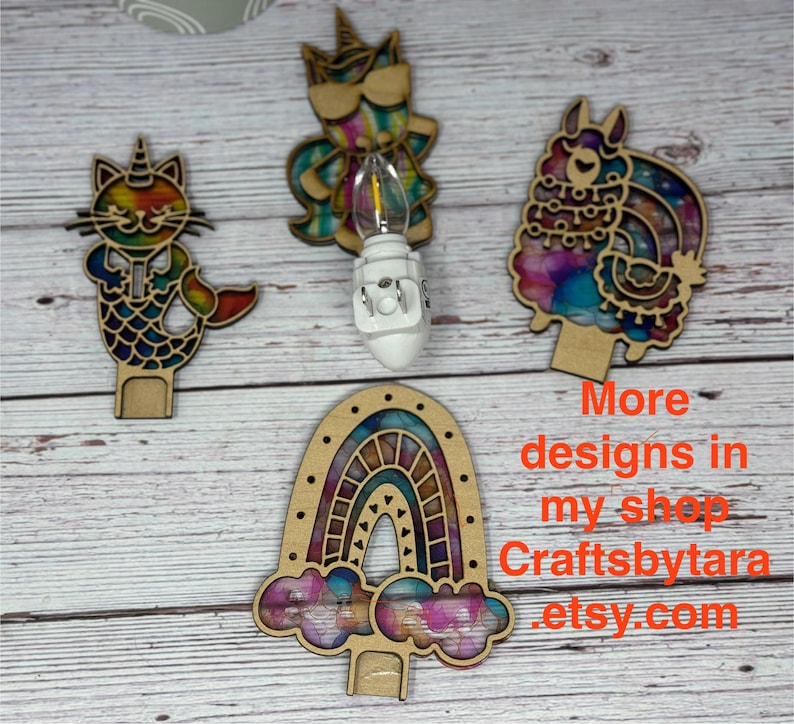 May include: Wooden night light designs featuring a cat-mermaid, unicorn, llama, and rainbow. Each design has a colorful, stained-glass effect. The text "More designs in my shop Craftsbytara etsy.com" is visible.