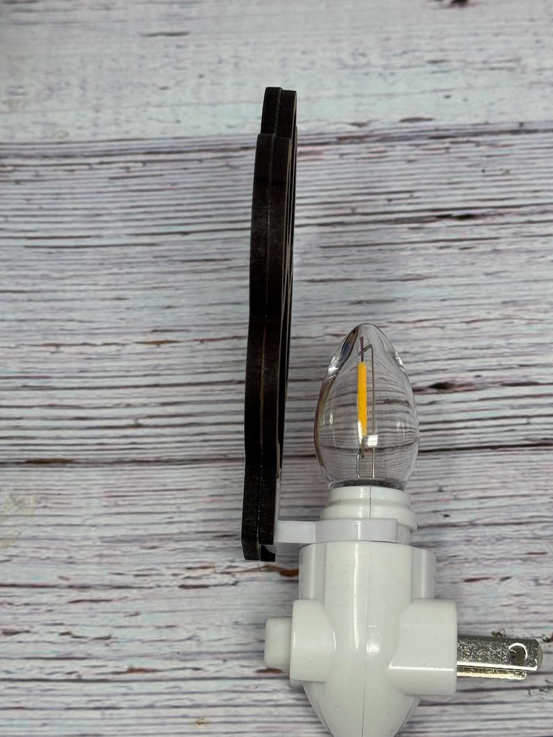 May include: A white night light with a clear, teardrop-shaped bulb containing a yellow filament. A dark brown, decorative element is attached to the side. The night light has a standard two-prong plug.