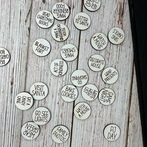 May include: A set of 20 white wooden circles with black text, each circle featuring a different Christmas activity. The activities include "Make Food", "Make S'mores", "Watch a Movie", "Decorate House", "Visit Santa", "Go See Lights", "Family Photos", "Bake Cookies", "Game Night", "PJ Day", "Read Christmas Books", "Open Gifts", "Letter to Santa", "Blanket Fort", "Act of Kindness", "Wrap Presents", "Sing Carols", "Eat Candy Cane", "Wear Green", "Write Wish List".