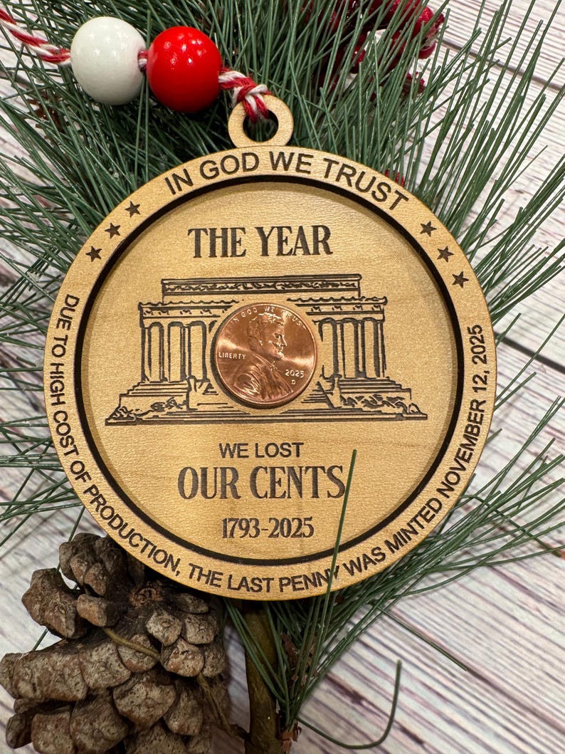 May include: Wooden Christmas ornament with a penny at the center, featuring the text "IN GOD WE TRUST" and "THE YEAR." The ornament includes the text "WE LOST OUR CENTS 1793-2025" and "DUE TO HIGH COST OF PRODUCTION, THE LAST PENNY WAS MINTED NOVEMBER 12, 2025."