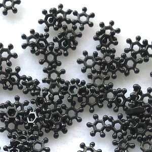 May include: A scattering of small, black metal charms shaped like a chemical molecule. The charms are arranged in a random pattern on a white background.
