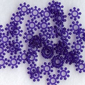 May include: A group of purple plastic star-shaped embellishments with a small circle in the center. The embellishments have a raised design of small dots around the circle.