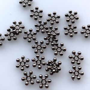 May include: A scattering of black metal snowflake-shaped beads. The beads have a small hole in the center for stringing.