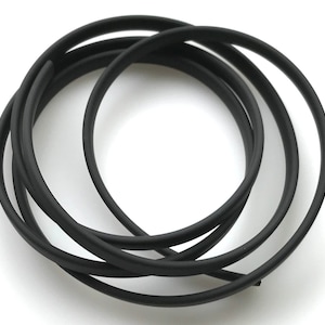 May include: Black heat shrink tubing, a type of electrical insulation, is coiled in a circle. The tubing is flexible and can be used to protect wires and cables from damage.