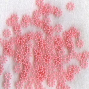 May include: A large group of pink plastic star-shaped beads. The beads are scattered on a white surface.