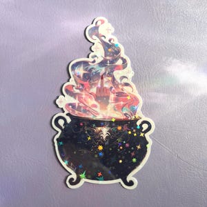 May include: A holographic sticker featuring a black cauldron with ornate patterns and colorful star accents. Rising from the cauldron is a swirling, multi-colored vapor cloud with a hand emerging from the center, displaying a middle finger gesture.