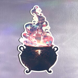 May include: A die-cut sticker featuring a black cauldron with ornate scrollwork patterns. Rising from the cauldron is a swirling, colorful cloud of pink, purple, and blue smoke with small star accents. A hand emerges from the smoke, gesturing.