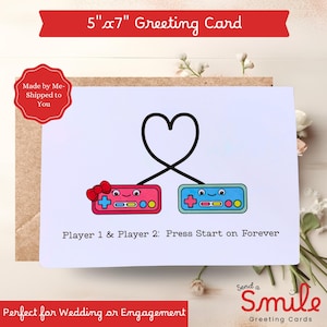May include: A 5" x 7" greeting card with a white background features two cartoon game controllers, one pink and one blue, connected by a heart. The text reads "Player 1 & Player 2: Press Start on Forever."