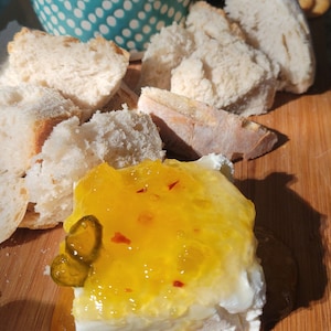 Peut inclure: Une planche en bois avec un fromage blanc recouvert de marmelade orange et un cornichon vert. Il y a des morceaux de pain blanc et un bol bleu avec de la marmelade verte sur la planche.