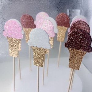 May include: A set of 10 ice cream cone cupcake toppers. The cones are gold glitter and the ice cream scoops are pink, white, and brown glitter.