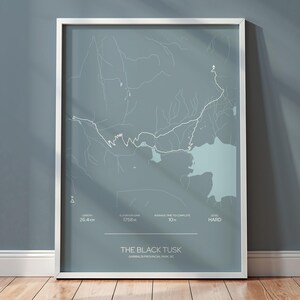 May include: A framed print featuring a map of The Black Tusk in Garibaldi Provincial Park, BC. The map is in shades of gray and white, with details of the trail and surrounding areas. The frame is white, and the print is displayed against a gray wall.