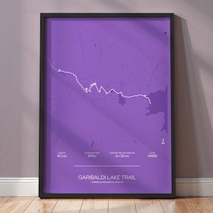 May include: A framed purple print of the Garibaldi Lake Trail map. The map features a white trail line and text indicating the trail's length of 18.2 km, elevation gain of 979m, and average time to complete of 6:30 hours. The difficulty level is marked as "HARD".