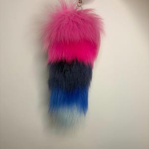 May include: A plush faux fur tail accessory featuring a gradient color pattern that transitions from a vibrant hot pink at the top, through dark navy blue, into a bright royal blue, and ending in a pale light blue at the pointed tip.