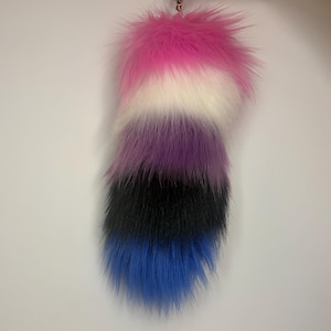 Puede incluir: Un accesorio de cola de piel sintética afelpada con un diseño de bloques de color horizontales. Las fibras largas y suaves pasan de un rosa vibrante en la parte superior, seguido de blanco, morado, negro y una punta azul brillante, con un cierre metálico.
