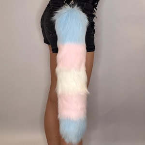 May include: A fluffy, layered tail accessory in pastel colors. The tail is attached to a silver clasp and features sections of light blue, pink, and white faux fur. The accessory is designed to be worn as a fashion statement.