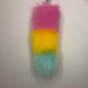 Può includere: Un lungo accessorio a coda in pelliccia sintetica felpata con un vivace design a gradiente tricolore. La sezione superiore è rosa brillante, che sfuma in un giallo vivido al centro e termina in una base di colore verde menta tenue.