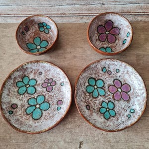 May include: Set of four ceramic bowls with a white background and floral designs. The bowls feature blue and purple flowers with white centers. The bowls are perfect for serving snacks or desserts.