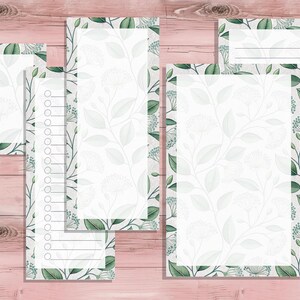 May include: A collection of stationery items, including notepads and list pads, featuring a delicate floral pattern in shades of green and white. The stationery is arranged on a pink wooden surface.