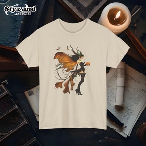 Puede incluir: Una camiseta blanca con un estampado gráfico de una mujer con alas y cuernos sosteniendo una calabaza. La mujer lleva un vestido negro y tiene el pelo largo y negro.