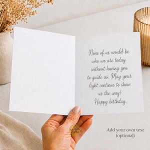 May include: A white greeting card held open, featuring black cursive text that reads: None of us would be who we are today without having you to guide us. May your light continue to show us the way! Happy birthday. The card includes an optional text area.