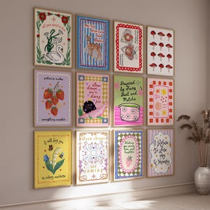 May include: A gallery wall featuring twelve rectangular framed art prints with various illustrations including a swan, a deer, mushrooms, strawberries, a snail, a matcha bowl, and floral motifs, each containing unique handwritten text in colorful designs.