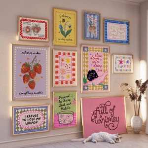 May include: A gallery wall featuring ten framed art prints with colorful illustrations and text, including phrases like 'patience makes everything sweeter', 'slow down you're doing fine', and 'full of whimsy', displayed on a light wall above a white floor.