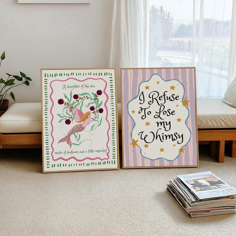 May include: Two rectangular framed wall art prints. The left print features a mermaid illustration with the text A daughter of the sea, made of seafoam and a little mischief. The right print has purple stripes and the text I Refuse To Lose my Whimsy.
