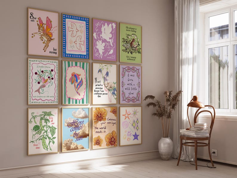 May include: A gallery wall featuring twelve rectangular framed art prints with various illustrations and text, including phrases like Stay soft but strong, Here comes the sun, and Embrace your own light, the world needs it, displayed in a grid arrangement.