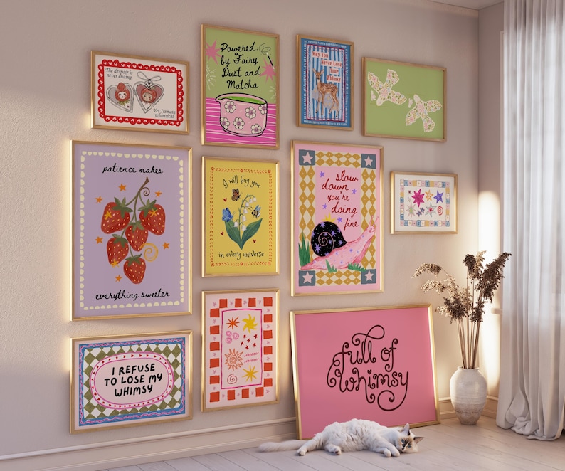 May include: A gallery wall featuring eleven framed art prints with various illustrations and text, including phrases like 'Powered by Fairy Dust and Matcha', 'patience makes everything sweeter', 'slow down you're doing fine', and 'full of whimsy'.