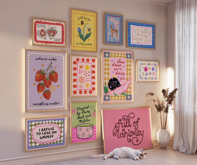 May include: A gallery wall featuring ten framed art prints with colorful illustrations and text, including phrases like 'patience makes everything sweeter', 'slow down you're doing fine', and 'full of whimsy', displayed on a light wall above a white floor.