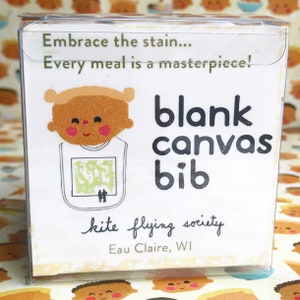 May include: A white and brown illustrated baby bib with the text "blank canvas bib" and "kite flying society Eau Claire, WI". The bib has a green and brown stain on it, and the text "Embrace the stain... Every meal is a masterpiece!" is at the top.