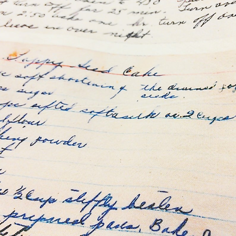 May include: Close-up of a handwritten recipe for Poppy Seed Cake on lined paper. The recipe includes ingredients like shortening, sugar, flour, and baking powder. The text is written in blue ink.