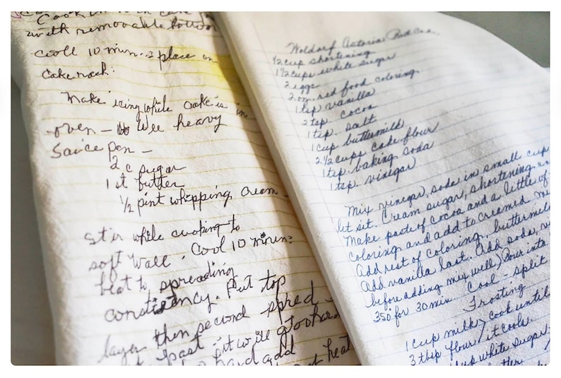 May include: A close-up of a handwritten recipe book with two pages open. The left page has instructions for making a cake, including the ingredients and steps. The right page has instructions for making a Waldorf Astoria cake, including the ingredients and steps. The pages are yellowed with age and the handwriting is in black ink.