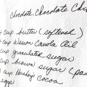 May include: Handwritten recipe for chocolate chip cookies, listing ingredients including butter, canola oil, granulated sugar, brown sugar, and cocoa.