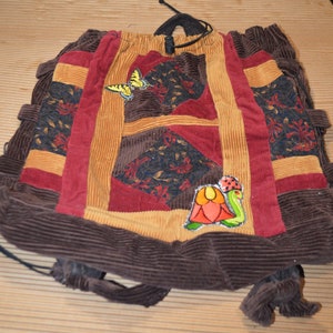 May include: A brown corduroy drawstring bag with a patchwork design. The bag features a yellow butterfly, a red flower, and a green ladybug.
