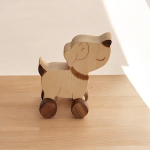 May include: A wooden toy dog with a smiling face and brown wheels. The dog is light brown and has a dark brown collar.