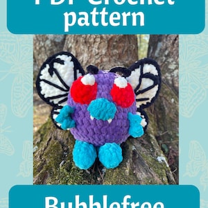 Puede incluir: Una criatura de ganchillo morada con ojos rojos, detalles turquesa y alas blancas y negras. La imagen incluye el texto "PDF Crochet pattern" y "Bubblefree". El peluche está sentado en un tronco de árbol.