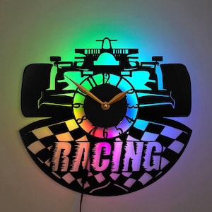 May include: A black vinyl record clock with a racing car design and a checkered flag pattern. The clock face is rainbow colored and the hands are gold. The clock is illuminated with colorful LED lights. The word "RACING" is printed on the clock face.